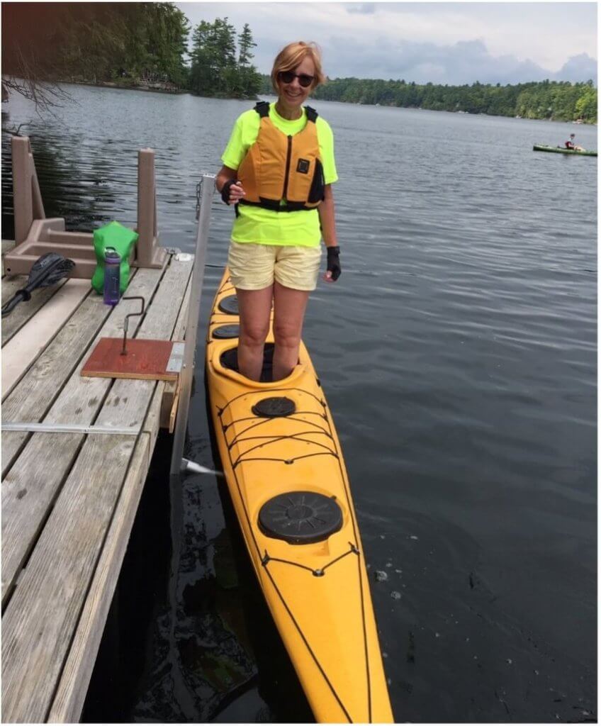 woman standing in a yellow kayak beside a dock using KayaArm to balance